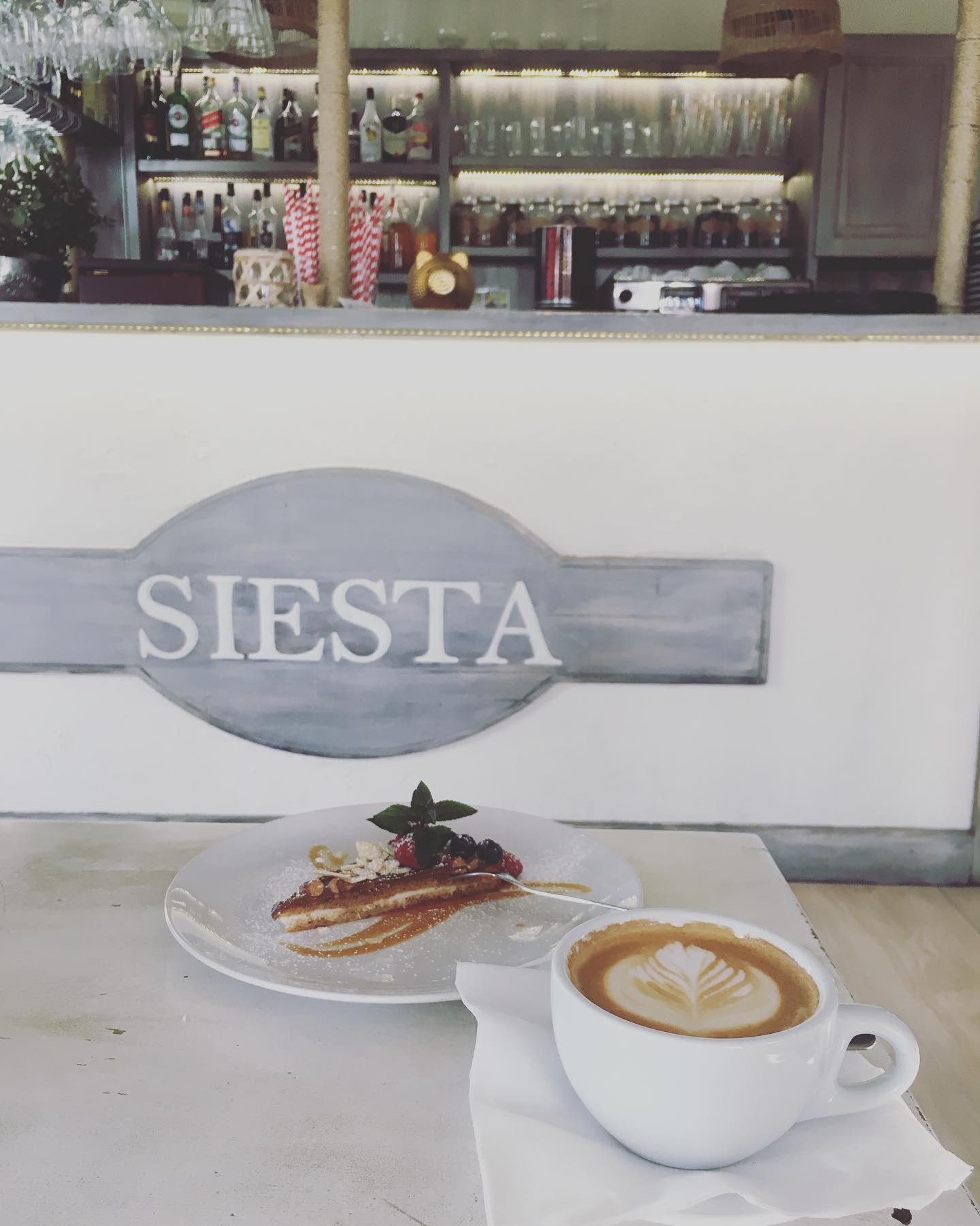 Cappuccino latte art z ciastem owocowym na tle baru Siesta